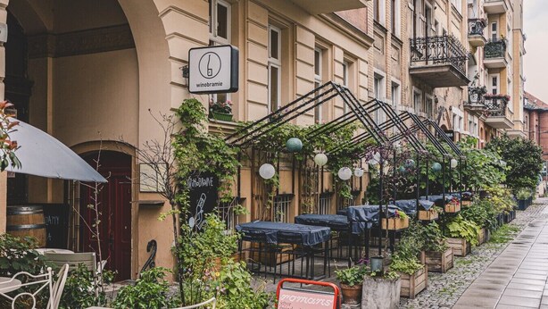 Una hilera de mesas y sillas al aire libre, un cartel para un bar de vinos y un edificio con balcones.