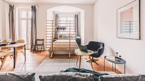 Una sala moderna con comedor, una cama con cabecera de madera, una laptop sobre una mesita y un cuadro en la pared.