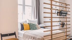 Un dormitorio con cama, almohadas, un perchero de madera con cubos, una ventana y vistas al exterior.