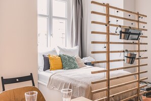 A bedroom with a bed, pillows, a wooden rack with buckets, a window, and a view of the outside. - Diente | Studio | Poznań Jeżyce | Balkon & Kamienica (Poznań)