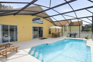Une piscine avec un patio couvert, une table et des chaises, ainsi quâun barbecue.