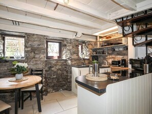 A kitchen with stone walls, a dining area with a table and chairs, and a countertop with kitchen appliances. - Merrion cottage, Penmachno (Betws-y-Coed)
