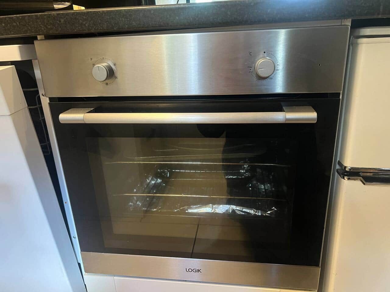 Um forno de aço inoxidável com porta de vidro e painel de controle com configurações de temperatura, e a marca 'LOGIK' na frente.