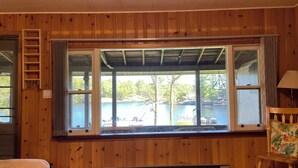 Una habitación con paredes de madera, un ventanal con vista a un lago, un banco de madera y una mesa.
