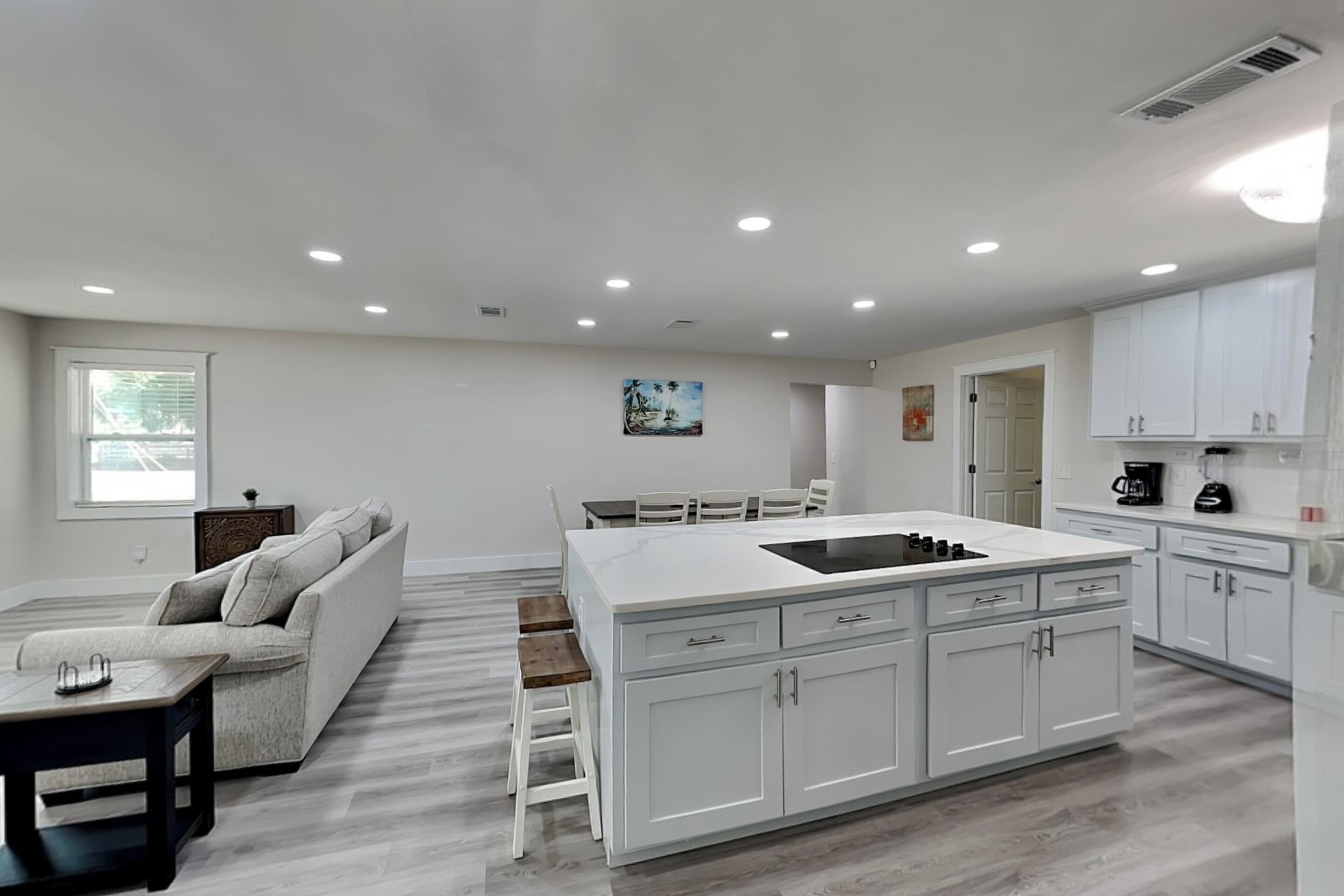 A modern kitchen with white cabinetry, a central island, and a dining area with a sofa and chairs.