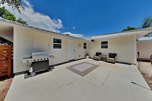 A covered patio area with a grill, two chairs, and a small table. - Turtle Dove (Panama City Beach)