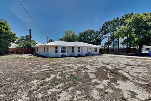 A single-story house with a flat roof, a front porch, and a backyard with sparse vegetation. - Turtle Dove (Panama City Beach)