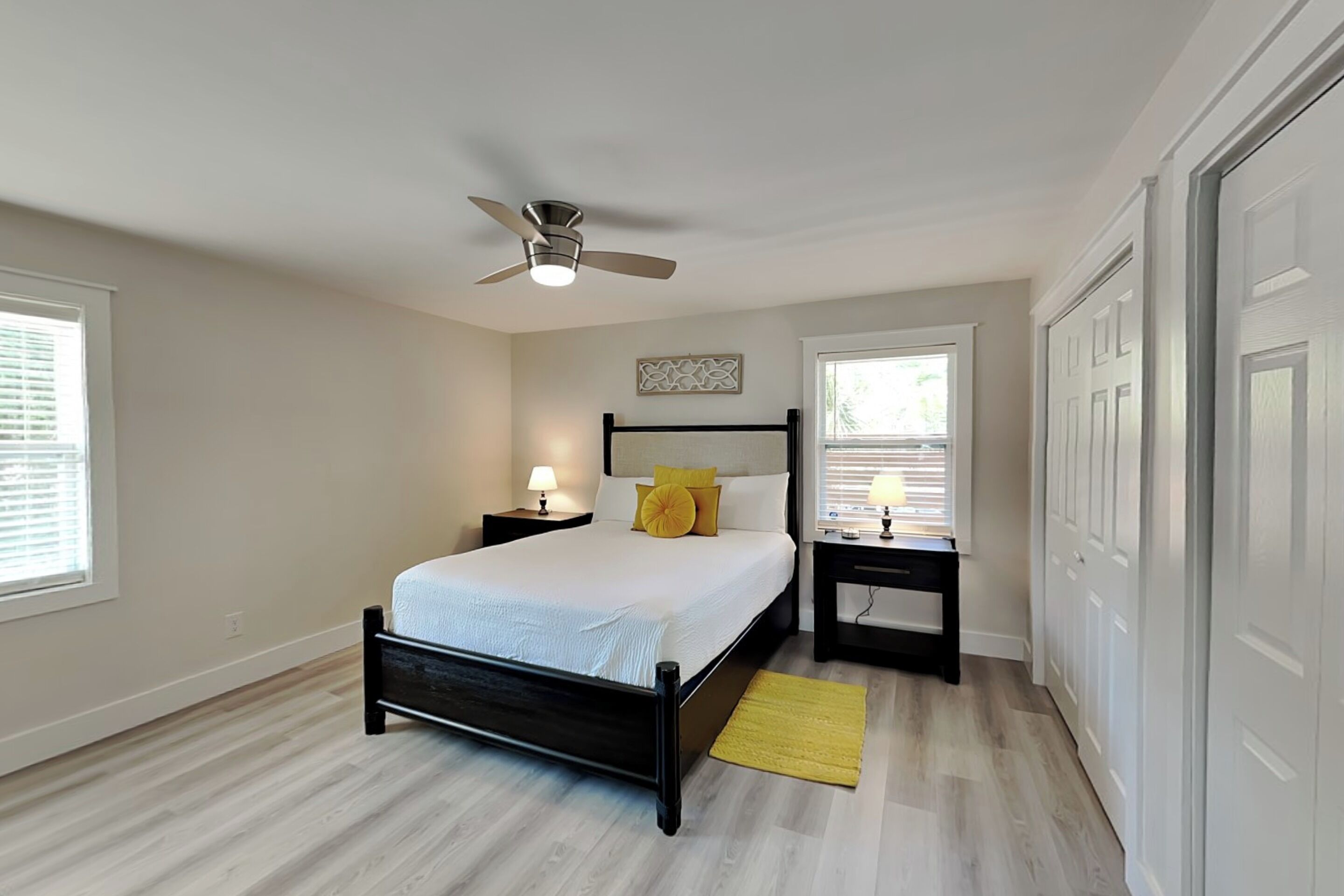 Ein Schlafzimmer mit Bett, Deckenventilator, Nachttischen, Fenster und Tür.