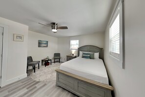 A bedroom with a bed, a chair, a nightstand, a ceiling fan, and a window. - Turtle Dove (Panama City Beach)
