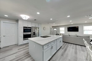 A modern kitchen with white cabinetry, a central island, and built-in appliances. - Turtle Dove (Panama City Beach)