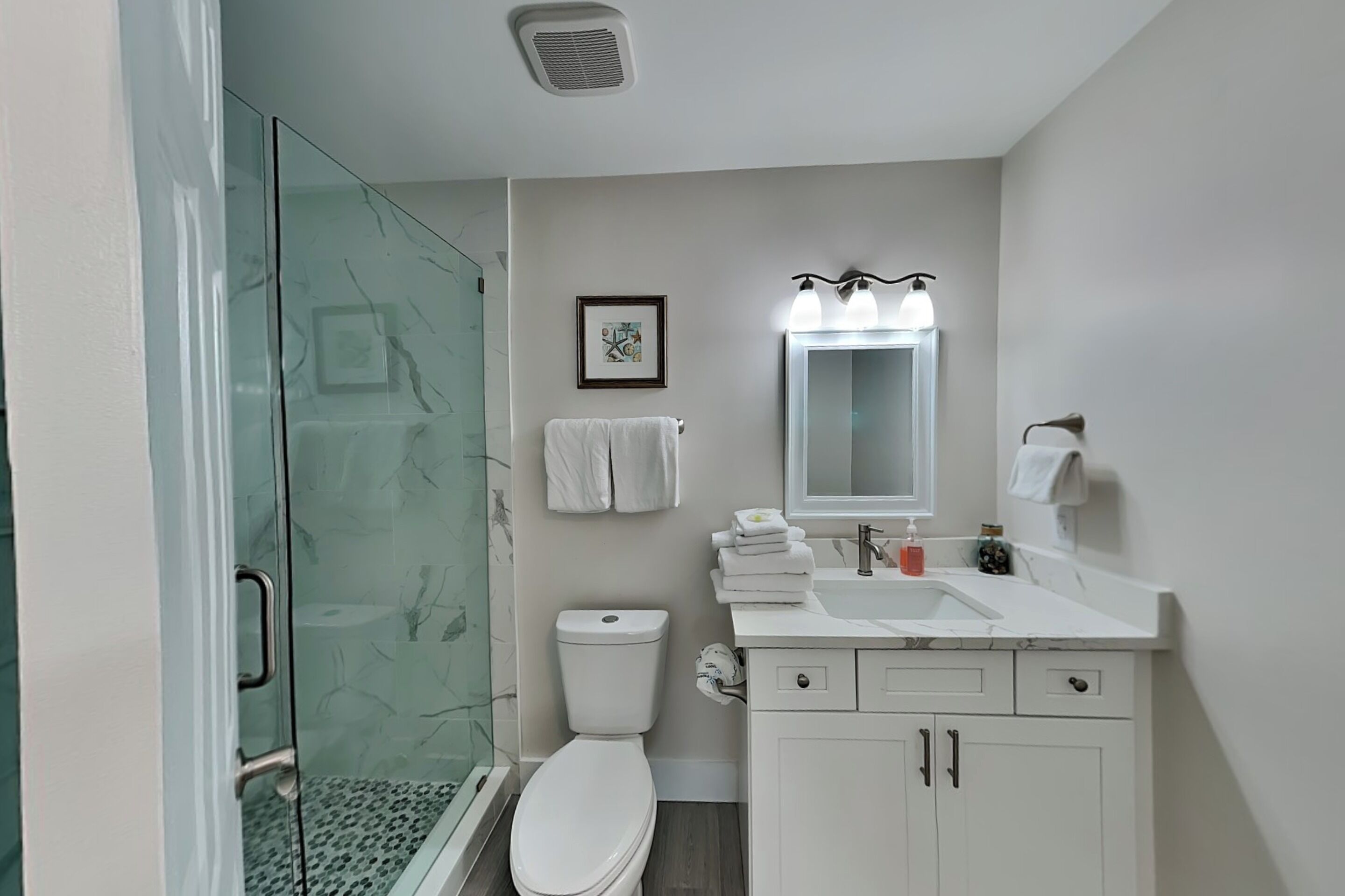 Un baño moderno con cabina de ducha de vidrio, inodoro, lavabo con espejo y perchero para toallas.