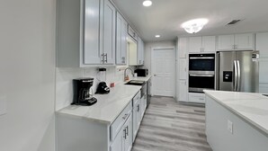 Una cocina moderna con armarios blancos, horno integrado, refrigerador y cafetera.