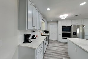 A modern kitchen with white cabinets, a built-in oven, a refrigerator, and a coffee maker. - Turtle Dove (Panama City Beach)