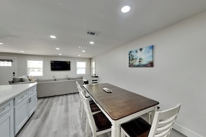 A modern kitchen with white cabinetry, a wooden dining table, and a gray sofa. - Turtle Dove (Panama City Beach)