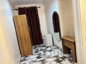 A bathroom with a wooden door, a white refrigerator, a wooden vanity, and a shower with a curtain. - KELNESSA HOTEL (Obuasi)