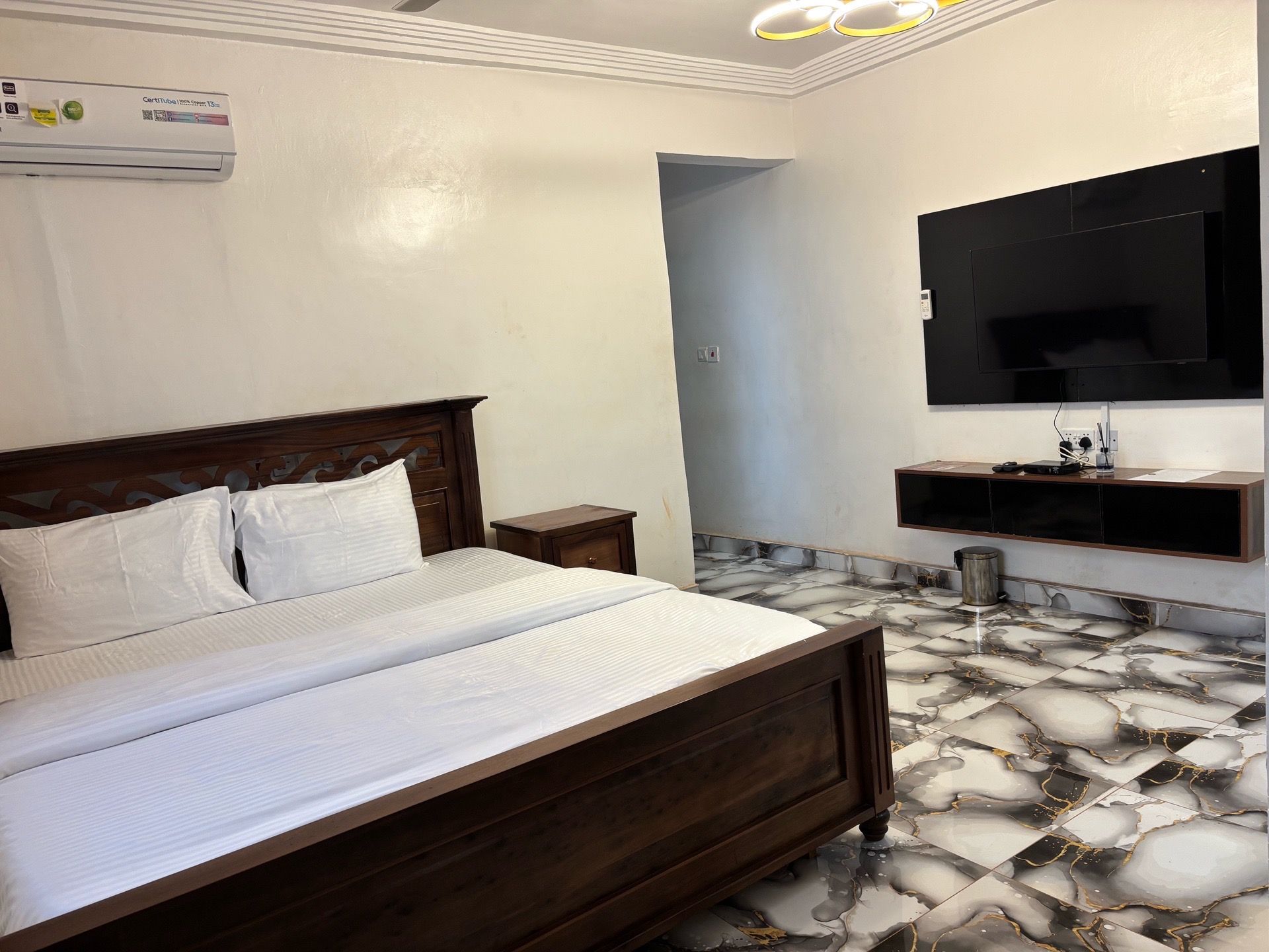 A hotel room with a bed, a TV mounted on the wall, and a marble-patterned floor.