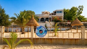 A beachside villa with a signboard, palm trees, and a fence. - Plage Blue Lagoon | Ocean View Penthouse (Mbour)