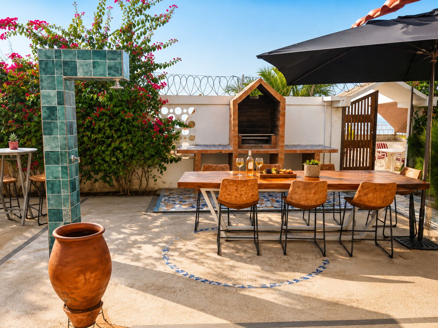 An outdoor patio with a wooden table, chairs, a grill, and a large planter.