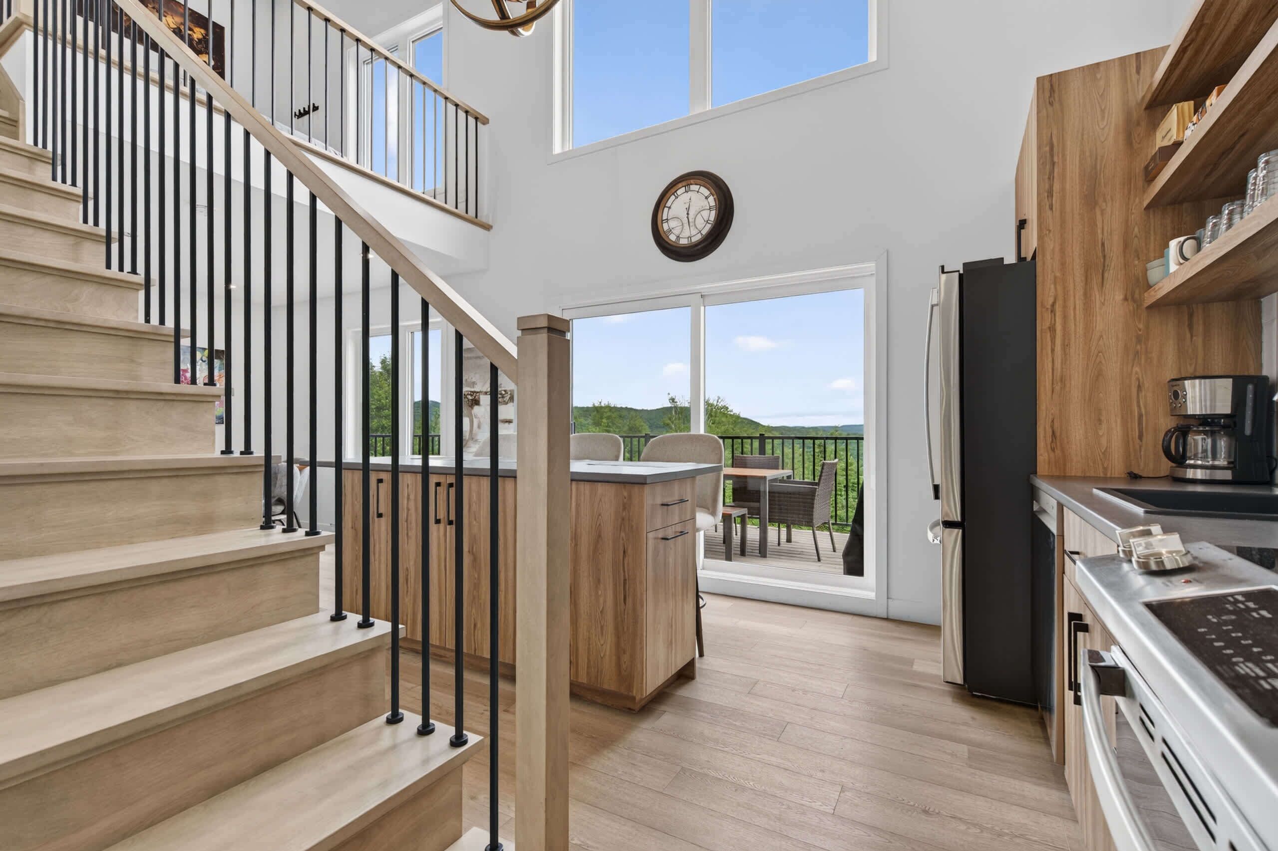 A modern kitchen with a wooden island, a dining area, and a staircase leading to an upper level.
