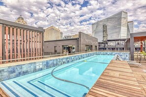 Ein Pool auf dem Dach mit klarem, blauen Wasser, umgeben von modernen Gebäuden und einer Holzterrasse.