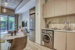 Eine moderne Küche mit integriertem Waschmaschine, eine Essecke mit Tisch und Stühlen sowie ein großes Fenster mit Blick ins Freie.