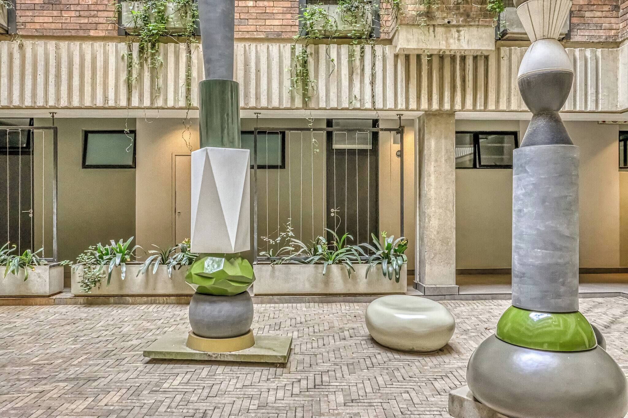 A courtyard with modern sculptures, potted plants, and a brick building in the background.