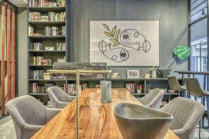 Moderni kirjasto, jossa on puinen pöytä, harmaalla kankaalla verhoillut tuolit ja hyllyt täynnä kirjoja.