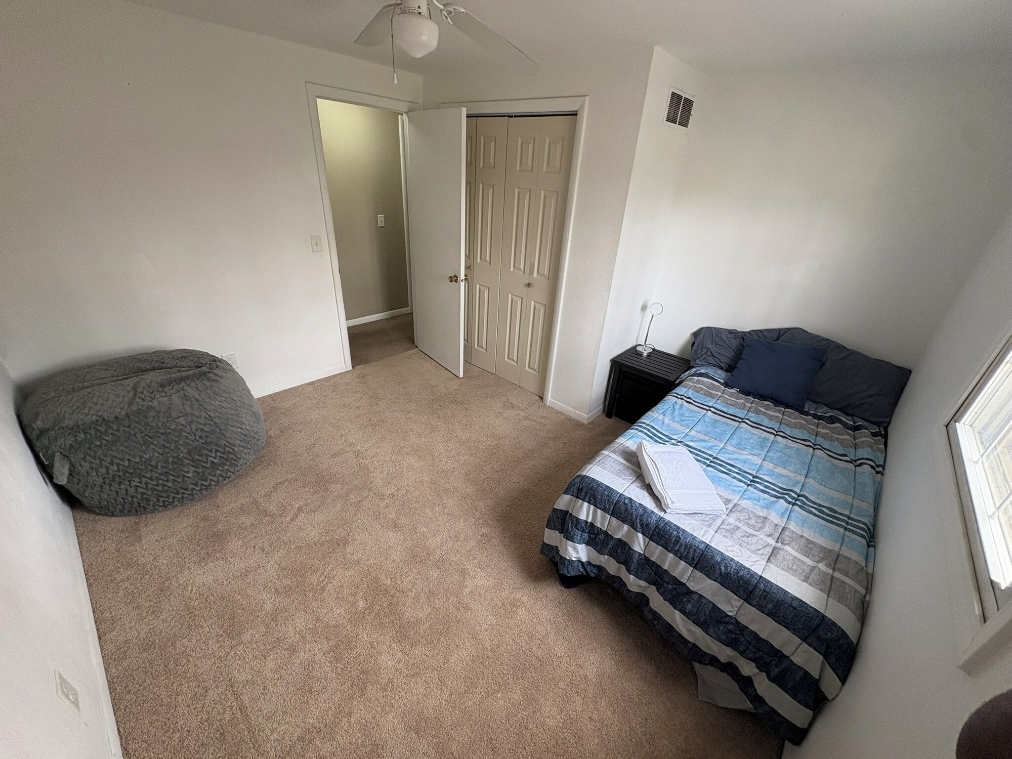 A bedroom with a bed, a bedside table, a chair, a door, and a ceiling fan.
