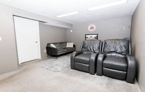 A room with a gray leather recliner, a gray sofa, a white door, and a framed picture on the wall. - Spacious 3BR w/ Hot Tub + FirePit (Toledo)