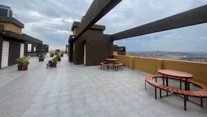 Une terrasse sur le toit agrémentée de plantes en pot, dotée de sièges extérieurs et offrant une vue sur le paysage urbain.