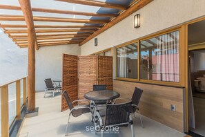 A covered outdoor area with a round table and chairs, wooden beams, and a glass partition. - Apart 500m From the Beach Pbs0101 (Mata de São João)