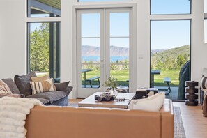 Uma sala de estar moderna com uma janela grande, um sofá, uma mesa de centro e vista para uma paisagem verde.