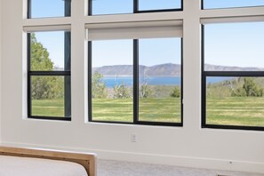 Ein Zimmer mit großen Fenstern, einem Bett und Blick auf ein grasbewachsenes Feld und Berge.