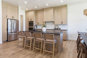 Une cuisine moderne avec des meubles en bois, un réfrigérateur en acier inoxydable, un îlot central doté de tabourets de bar et un vase rempli de fleurs.
