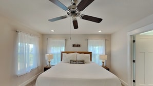 Ein Schlafzimmer mit einem Bett, Deckenventilator, zwei Nachttischen mit Lampen und einem Kissen mit der Aufschrift 'Beach Welcome'.