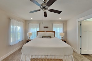 A bedroom with a bed, ceiling fan, two bedside tables with lamps, and a 'Beach Welcome' pillow. - Sweet Retreat (Pensacola)
