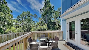 Eine Terrasse mit einem Tisch aus Glas und Korbstühlen, umgeben von einem Holzzaun, mit Bäumen und einem Gebäude im Hintergrund.