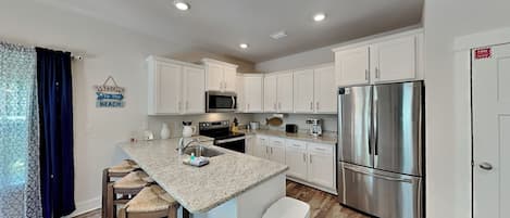 A modern kitchen with white cabinets, stainless steel appliances, a granite countertop, and a bar area with stools.