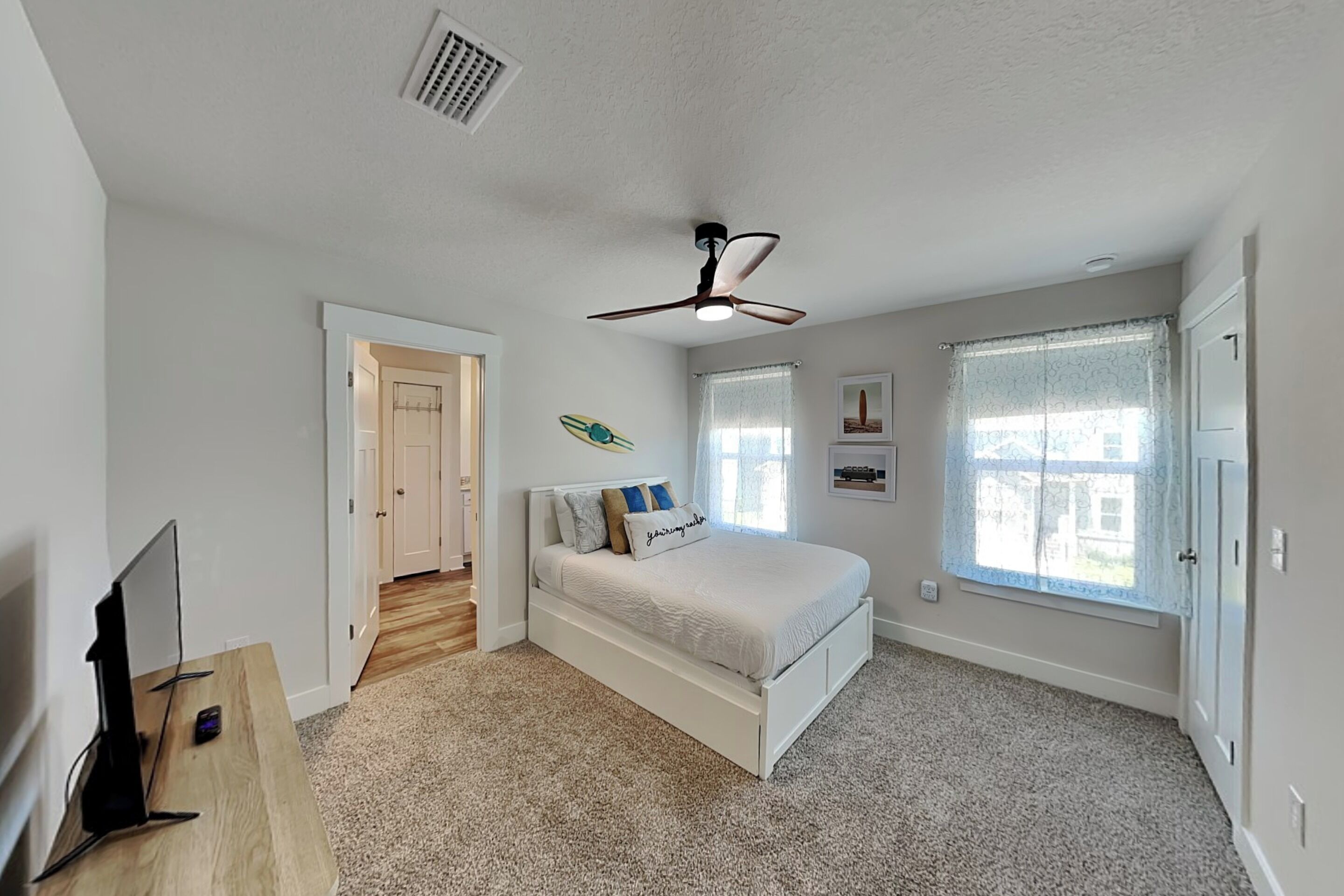 A bedroom with a bed, a ceiling fan, a TV, and a window.