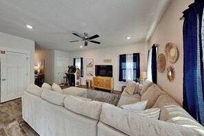 A living room with a sofa, television, ceiling fan, and decorative wall art. - Sweet Retreat (Pensacola)