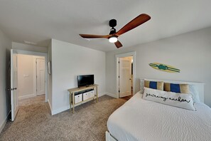 A bedroom with a bed, a ceiling fan, a television on a stand, and a door leading to another room. - Sweet Retreat (Pensacola)