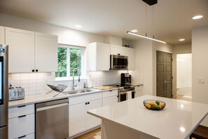 Una cocina moderna con armarios blancos, un refrigerador de acero inoxidable, un microondas, una cafetera y un lavabo.