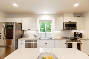 A modern kitchen with white cabinetry, stainless steel appliances, and a central island. - Basecamp - modern cabin with hot tub + sauna near Mount Rainier (Packwood)