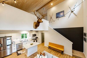 A modern kitchen with a central island, a dining area with a bench, and a mounted deer head. - Basecamp - modern cabin with hot tub + sauna near Mount Rainier (Packwood)
