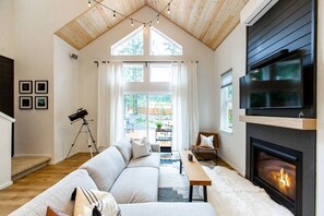 A spacious living room with a high ceiling, a fireplace, a large TV, and a cozy seating area. - Basecamp - modern cabin with hot tub + sauna near Mount Rainier (Packwood)
