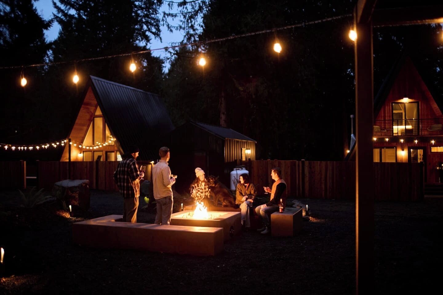 A rustic outdoor setting with a fire pit, wooden fences, and string lights.