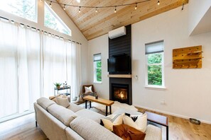 Ein modernes Wohnzimmer mit Kamin, großen Fenstern und einer Holzbalkendecke.