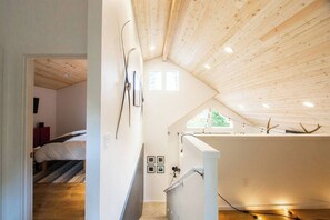 Ein Zimmer mit schrägem Dach, Holzbalken, einem Bett, einem Schreibtisch und einem Fenster mit Lichterkette.