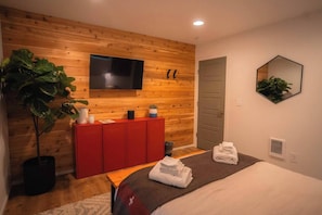 Une chambre moderne avec un mur en bois, un téléviseur, une armoire rouge, une plante et un lit avec des serviettes.