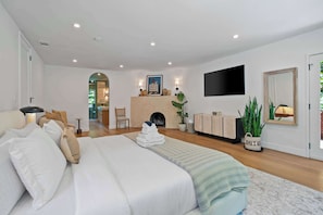 A modern bedroom with a large bed, a flat-screen TV, a fireplace, and a dining area. - Laurel Canyon 5BR | Pizza Oven + Fireplaces | C&C (Los Angeles)
